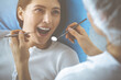 © rogerphoto - Smiling brunette woman being examined by dentist at dental clinic. Hands of a doctor holding dental instruments near patient's mouth. Healthy teeth and medicine concept