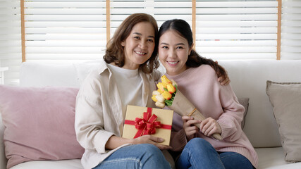 portrait attractive beautiful mum sit with grown up daughter give gift box and flower in family mome