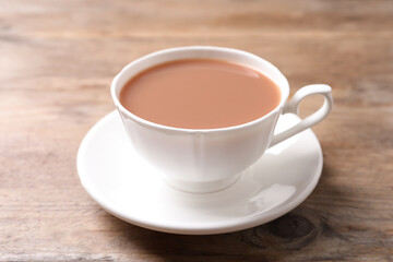 Poster - Delicious tea with milk in white cup on wooden table