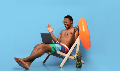 Shocked black guy chilling in lounge chair, looking at laptop, winning lottery or casino bet, finding online sale