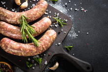 Bratwurst Or Sausages On Cutting Board With Spices At Black Table.