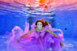 Underwater portrait of a beautiful young girl who swims and poses underwater in a purple dress. She looks at the camera and smiles. Concept. Horizontal orientation.