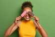 © wayhome.studio  - Photo of cheerful teenage girl has curly hair toothy smile enjoys life covers eyes with two delicious ice creams wears casual yellow t shirt feels happy during summer day isolated on green wall