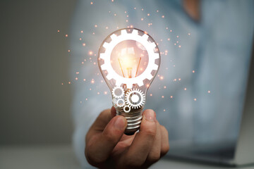 Poster - Businessman holding glowing lightbulb with mechanical gear , Creative thinking ideas and innovation concept.