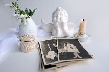 stack of vintage photos, pictures of children of first communion of 1950, candle is lit, spring flowers in vase, concept of family tree, genealogy, childhood memories