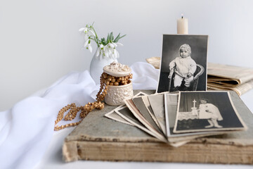 stack of vintage photos, pictures of children of first communion of 1950, candle is lit, spring flowers in vase, concept of family tree, genealogy, childhood memories