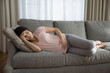 © fizkes - Unwell young Caucasian woman lying on couch touch baby bump feel unhealthy suffer from pain ache. Tired female relax on sofa touch baby bump have health problems during pregnancy. Healthcare concept.