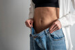 © Sergey - a slender woman with a bare stomach shows how she lost weight, holding her jeans with her hand. The concept of diet, weight loss, healthy lifestyle