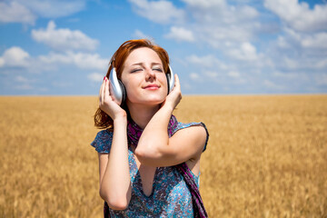 Wall Mural - Young  smiling girl with headphones at wheat field.