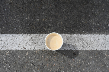 Take-away paper coffee cup on the white line of the asphalt road.