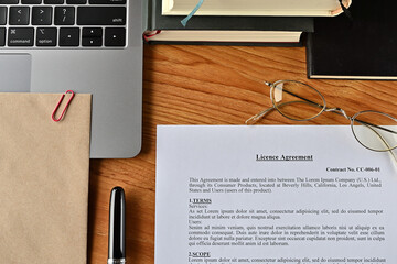 There is a dummy paper of Licence Agreement on the desk with a laptop, a pen and glasses.