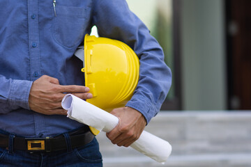 Engineer holding blueprint with yellow hard hat on site construction