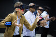 © JackF - Portrait of woman using virtual reality goggles gesturing standing in dark room with friends