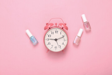 Wall Mural - Creative beauty layout. Alarm clock and bottles of nail polishes on a pink background. Top view. Flat lay