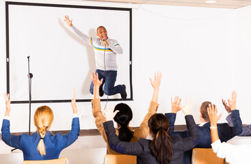 Wall Mural - Expressive emotional hispanic business coach speaking to audience and jumping on stage during public motivational training in conference room