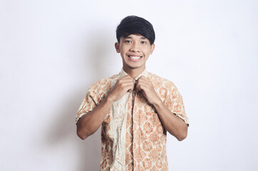 asian man wearing batik is buttoning his shirt while smiling