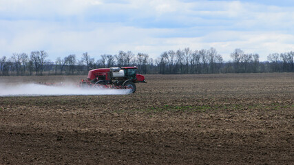 Red tractor with irrigation system watering a field on a cloudy day. agricultural machinery, work in the field. seasonal work. tractor fertilizes the ground