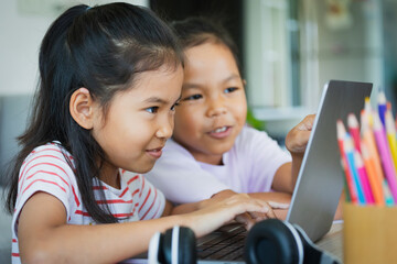 Two asian child girl students study online with teacher by video call together. Siblings are homeschooling with computer laptop during quarantine due to Covid 19 pandemic.