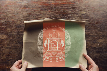 An old, frayed piece of paper with the Afghan flag on it lies on the scratched table.