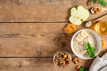 Wall Mural - Ingredients for cooking healthy breakfast. Oatmeal, dried and fresh fruits, honey and nuts on a wooden table with copy space top view. Breakfast table concept