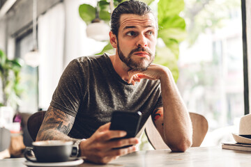 Handsome hipster man relaxing using digital smartphone and looking at screen typing message at table in cafe and restaurant,playing game online and social media