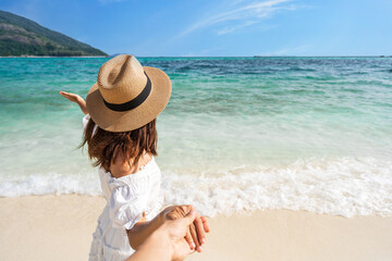 Wall Mural - Young couple traveler holding hands relaxing and enjoying at beautiful tropical white sand beach with wave foam and transparent sea, Summer vacation and Travel concept