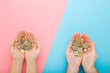 Opened young adult man and woman palms with euro coins on light blue pink table background. Pastel color. Point of view shot. Closeup. Compare income between husband and wife. Top down view.