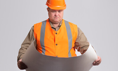 сonstruction worker in hard hat looking in with opened paper project in hands on grey studio background, engineer profession