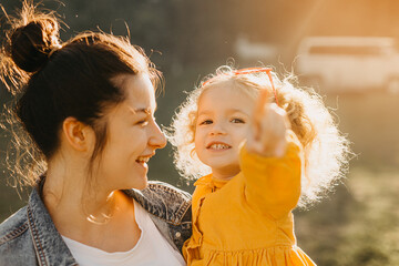 young pretty mom and cute curly daughter in nature under sunlight