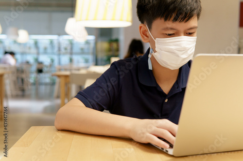The impact of the COVID-19 pandemic on adolescents. A smart asian teenager boy with face mask using laptop computer in a canteen. Online, Social distancing, Internet 5G, Technology, Restriction.