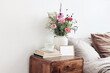 Cup of coffee and books on retro wooden bedside table. Blank greeting card mockup. White ceramic vase. Buquet of cosmos and zinnia flowers. Beige linen, velvet pillows in bed. Scandinavian interior.