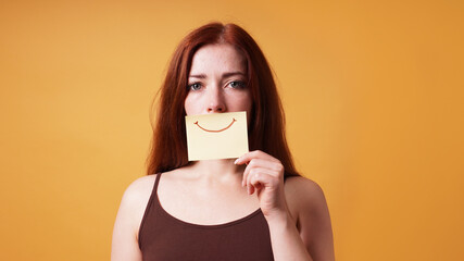 young woman hiding emotion with fake smile drawn on paper