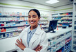© StratfordProductions - Cheerful young woman in labcoat standing with folded hands in chemist