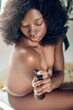 © zinkevych - Naked dark-skinned young woman applying body lotion on her body