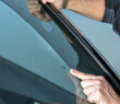 Car glass mechanic is pointing on a stone chip in a car windscreen.