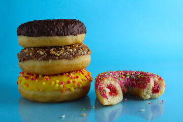 Wall Mural - Yellow pink chocolate donuts lie a stack of a row of cut-off bitten doughnut stuffed with pink chocolate on a blue bright background with room for text. still life from food