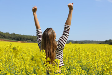 Wall Mural - Excited woman raising arms in a field in summer vacation