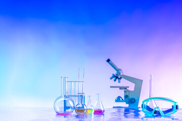 Poster - Flasks, a microscope, and safety glasses on a blue background. Chemical equipment near the place for the text. medical glassware and plastic safety glasses in scientific lab.