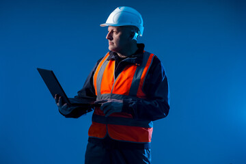 Poster - Portrait of an engineer or architect. Civil engineer with a laptop on a blue background. Worker face is brightly lit. Construction planning contractor. Developer of construction plans.