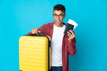 Young Brazilian man over isolated background in vacation with suitcase and passport