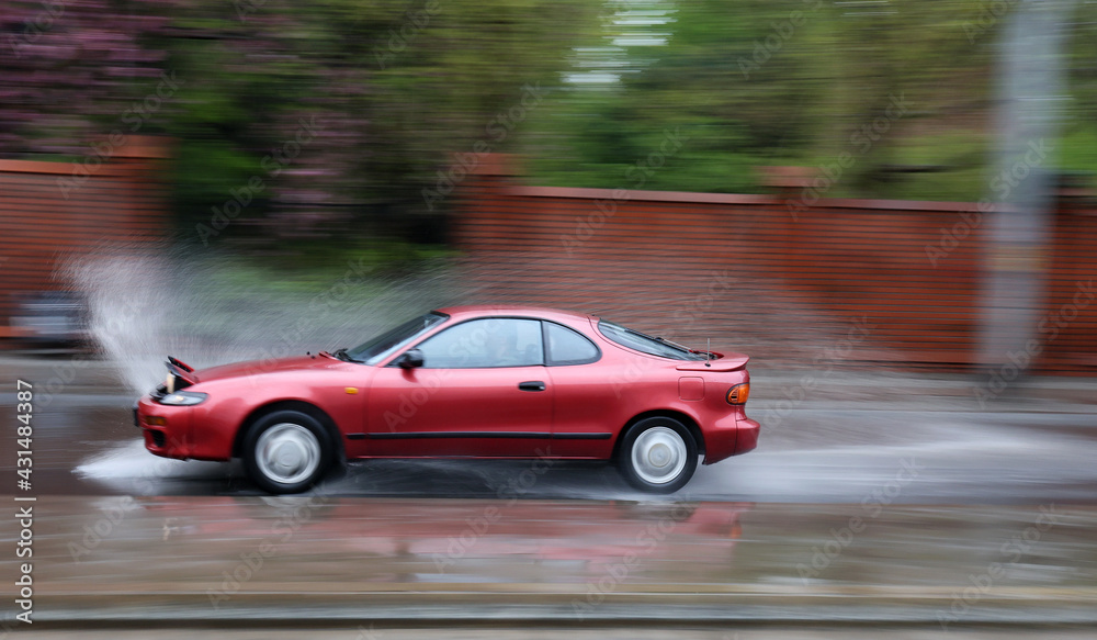 Samochód wpada w kałużę wody na jezdni powodująć rozbryzg.  - obrazy, fototapety, plakaty 