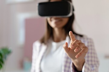 Canvas Print - Confident young woman in virtual reality headset pointing in the air while standing at her working place in office