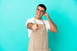 © luismolinero - Restaurant waiter man over isolated blue background making phone gesture and pointing front
