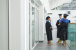 © Seventyfour - Wide angle view at group of young people wearing graduation gowns chatting indoors in modern college interior, copy space