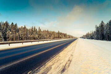 Wall Mural - Clear winter day, a country road passing through the coniferous forest. View from the side of the road