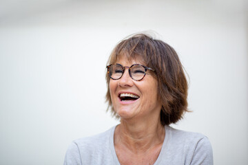 Wall Mural - Close up older woman laughing with eyeglasses against white background and looking away