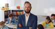 © TommyStockProject - Young male teacher standing in classroom with kids sitting at desk on background
