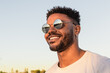 © Ana BG - Face portrait of a handsome black and young american man wearing sunglasses and smiling during sunset at the beach
