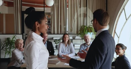 Wall Mural - Confident smiling young leader boss shaking hands with african american female employee, praising for excellent job results, showing respect and appreciation, promoting at group office meeting.