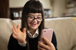 Cinematic shot of happy teen girl with down syndrome making video call with smartphone to friends or family at home. Concept of technology, handicapped, disability, media, friendship, new generation.